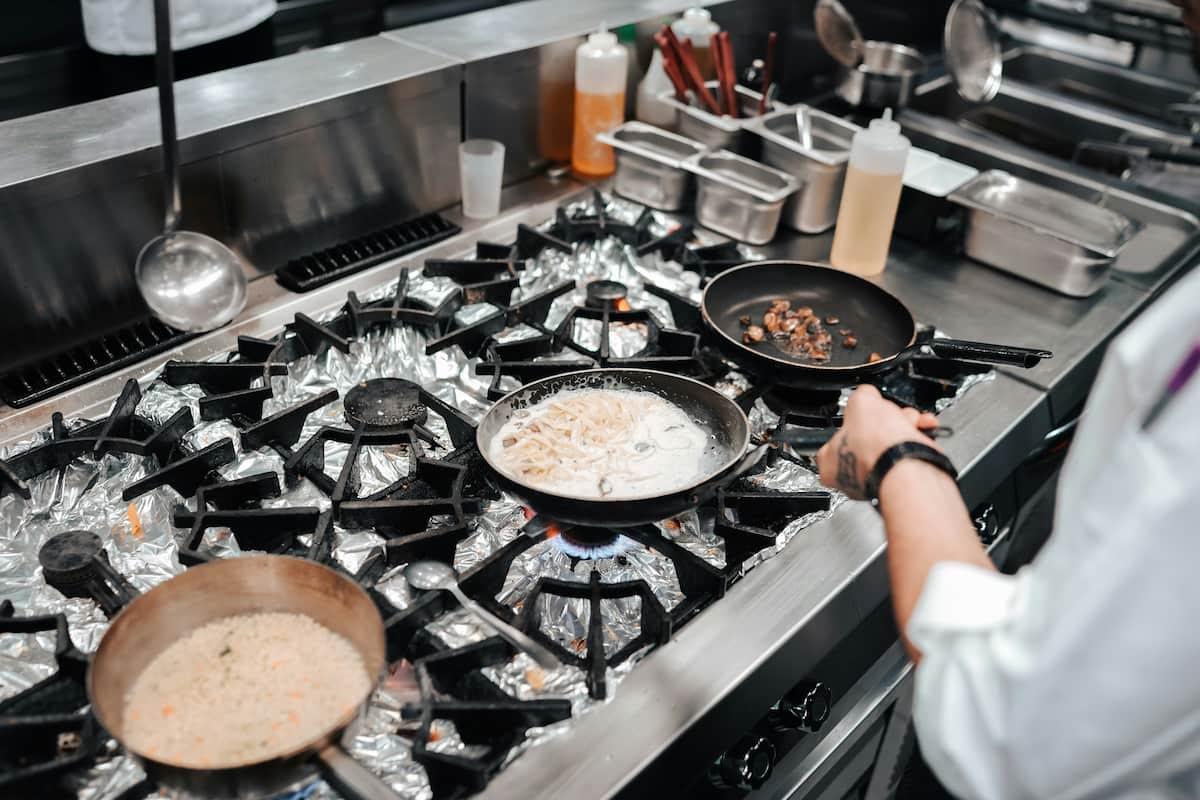 Pots cooking on a stove with foil-lined burners, possibly indicating restaurant health code violations in a commercial kitchen.
