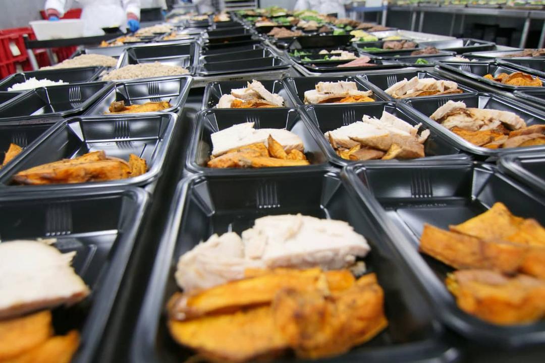 Pre-packaged meals on assembly line showing how to scale to a high volume kitchen efficiently and maintain quality.